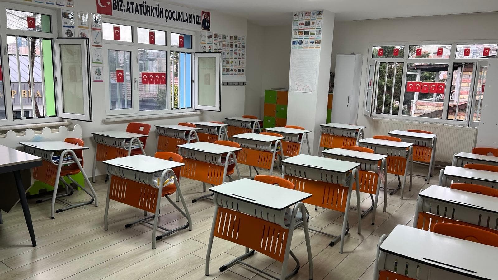 Aydınlık ilkokul dersliği — tekli sıralar ve “Biz Atatürk'ün Çocuklarıyız” panosu