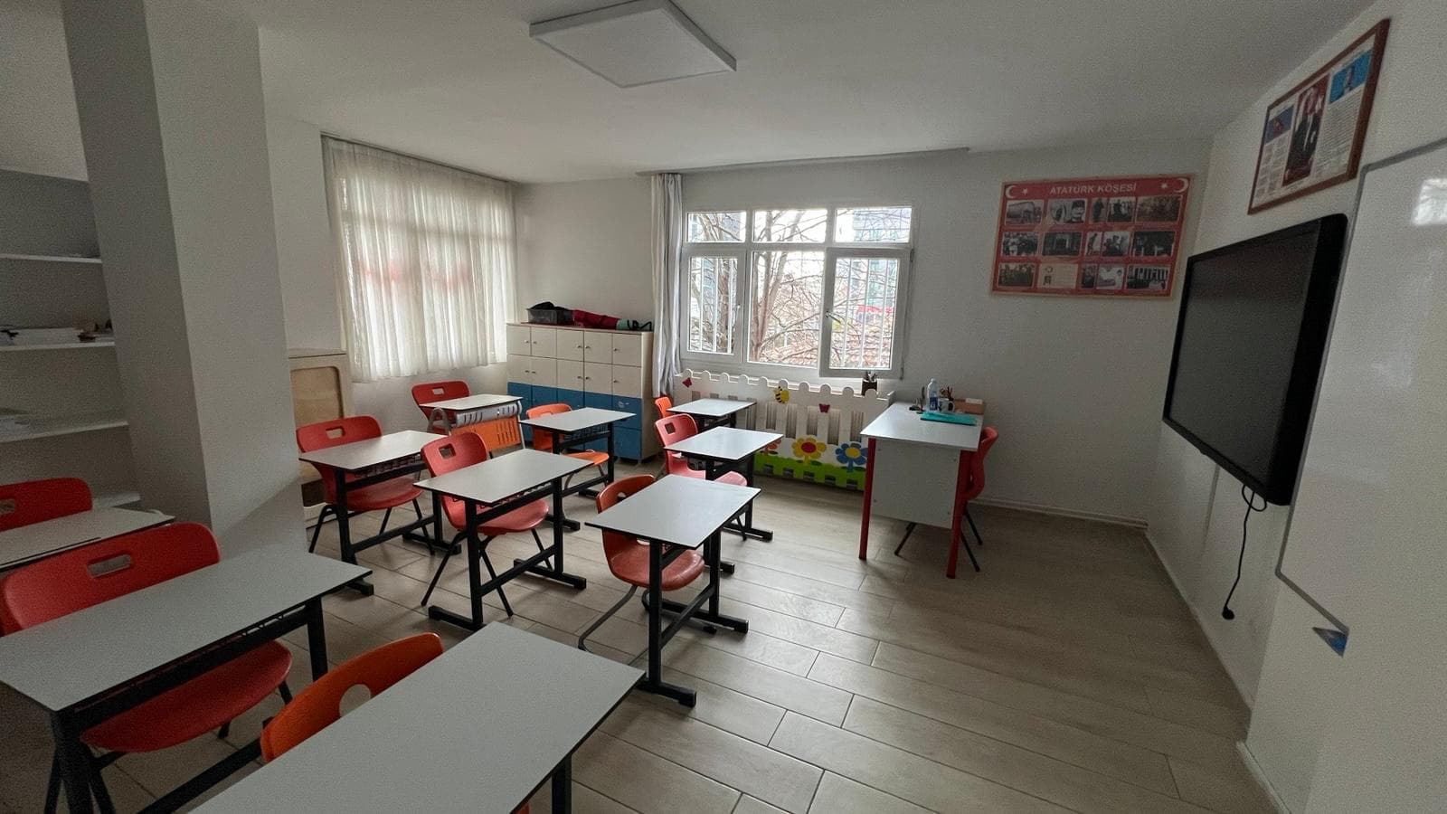 Ferah ilkokul sınıfı — kırmızı sandalyeler, akıllı tahta ve çiçekli korkuluk