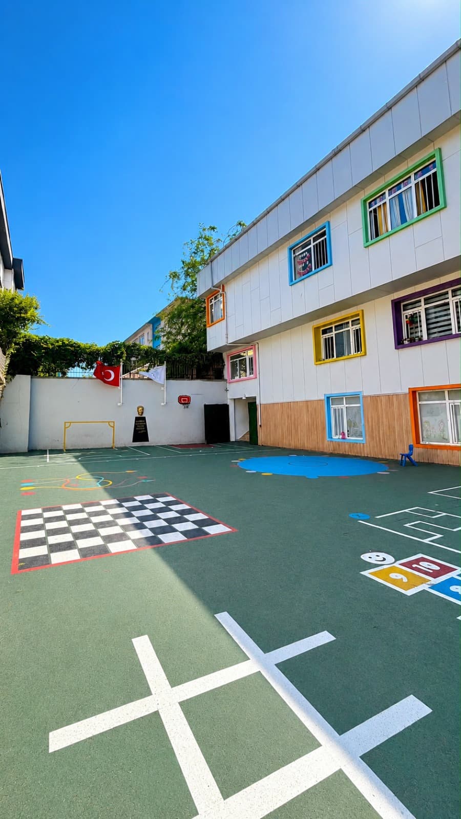 Açık hava oyun bahçemiz — satranç zemini, sek-sek ve renkli pencereli binamız